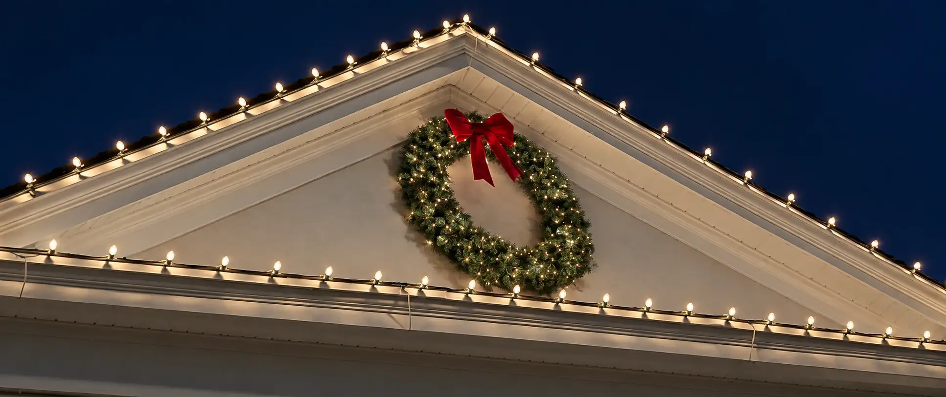 Gable end with warm-white C9 bulbs along the roofline and a lit wreath