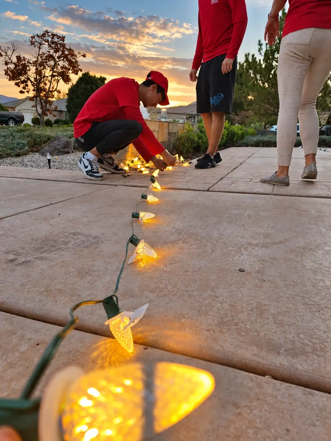 Glow Forward crew testing a strand of warm-white C9 bulbs on a driveway at dusk