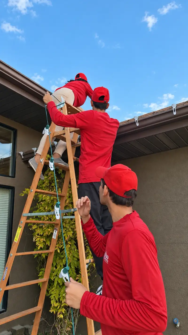 Glow Forward crew on a ladder clipping lights along a roofline