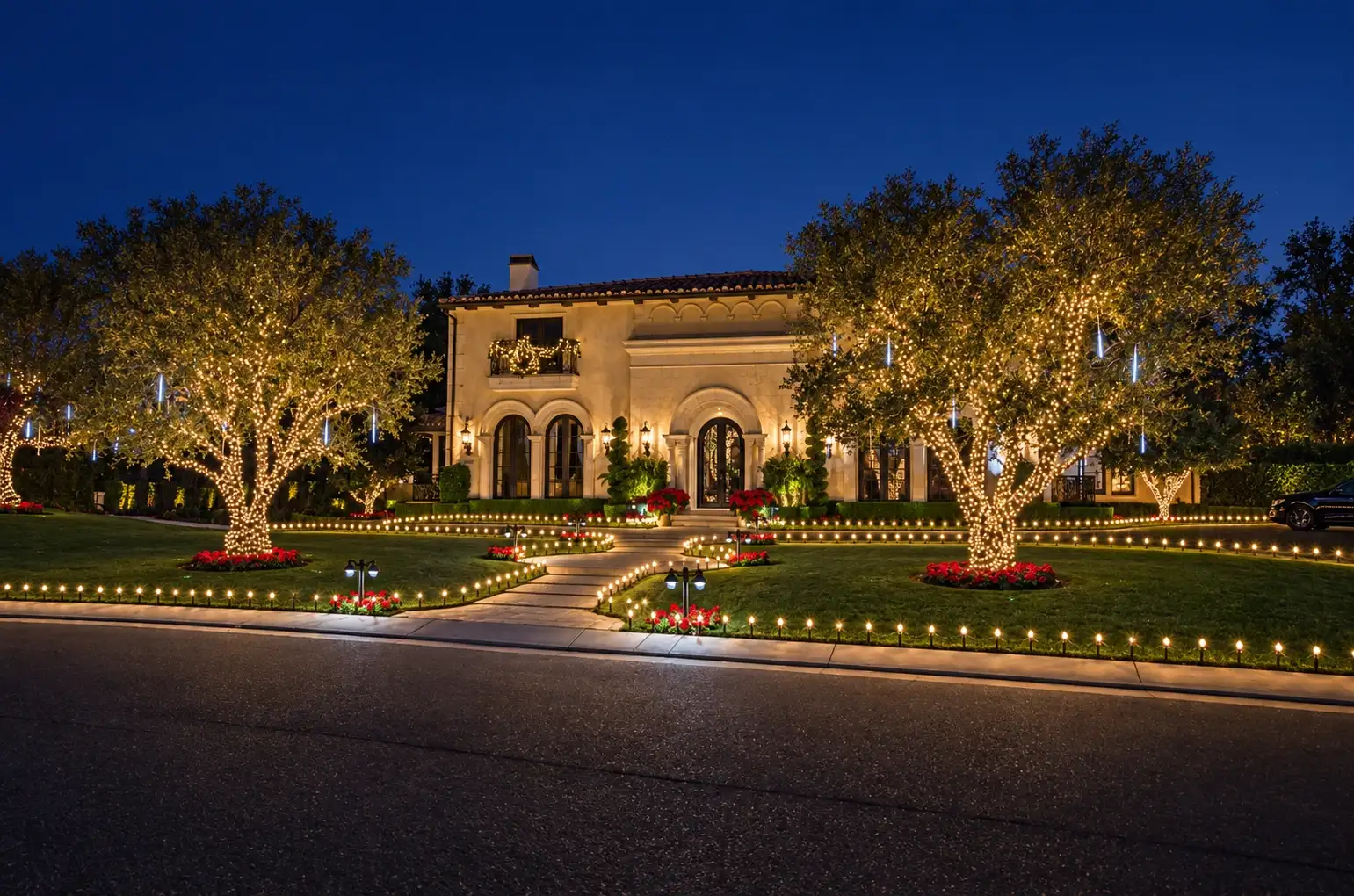 Estate home with lit trees and a lit driveway border at night