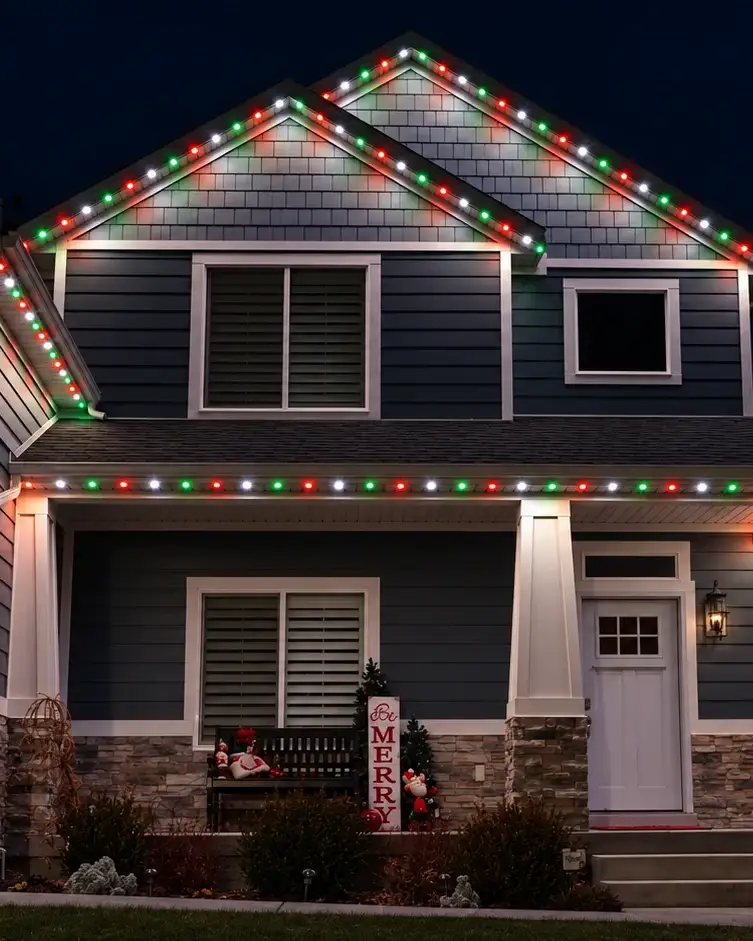 Example of permanent roofline lighting set to red, green and white along the gables of a two-story home at night