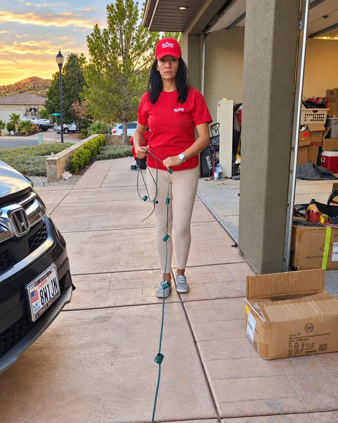 Glow Forward team member in a red branded cap and shirt laying out a strand of Christmas lights along a driveway