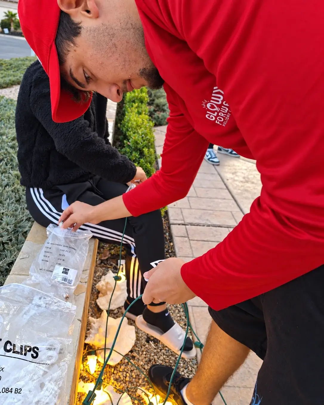 Glow Forward technician in a red branded cap and shirt sorting a bag of light clips and a strand of C9 bulbs